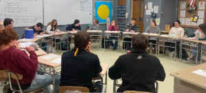 In this photo, students in the West Forest Literature and Interpretation course engage in a spirited peer-led debate with their teacher, Ms. Sarah Huth. 